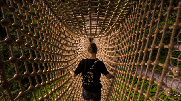 Eine dunkelbekleidete Person läuft über eine Hängebrücke.