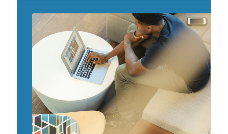 Employee sits in a modern seating area and types on his laptop.