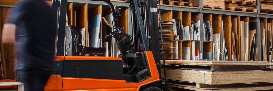 Mann läuft neben einem roten Stapler im Lager vorbei.